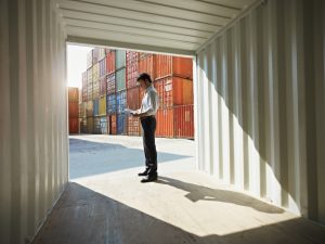 portrait of mid adult businessman standing near cargo container and writing on clipboard. Horizontal shape, side view, copy space